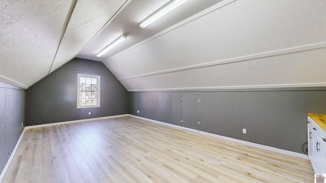 additional living space with a textured ceiling, light hardwood / wood-style floors, and vaulted ceiling