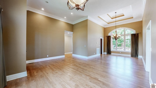 spare room with a raised ceiling, crown molding, light hardwood / wood-style flooring, and a notable chandelier