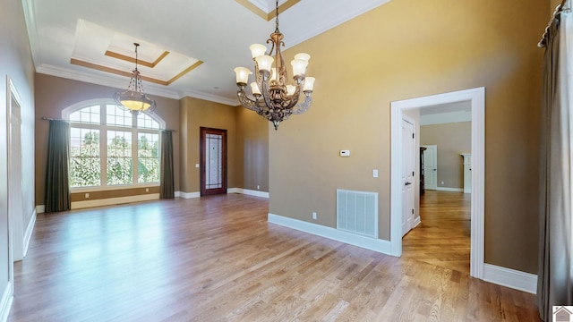 unfurnished room featuring a notable chandelier, a raised ceiling, light wood-type flooring, and crown molding