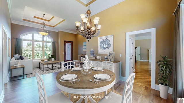 dining area with a tray ceiling, crown molding, wood-type flooring, and an inviting chandelier