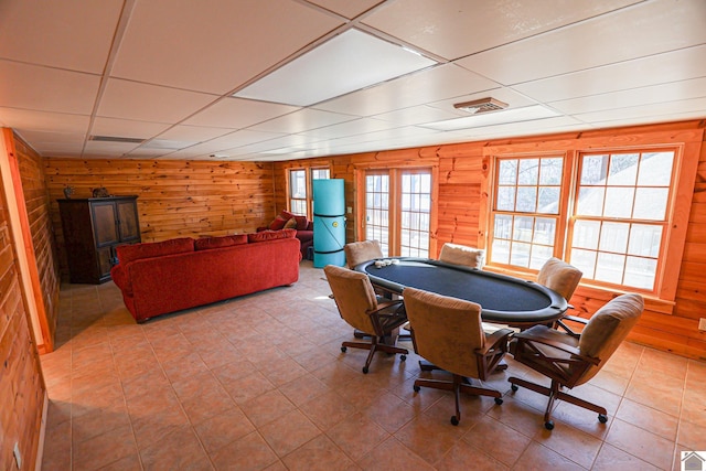 recreation room featuring wood walls, a drop ceiling, and light tile patterned floors