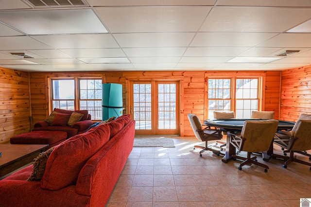 living room featuring a paneled ceiling, wood walls, light tile patterned floors, and a healthy amount of sunlight