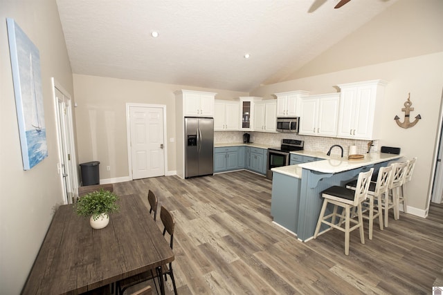 kitchen with lofted ceiling, backsplash, white cabinets, appliances with stainless steel finishes, and kitchen peninsula