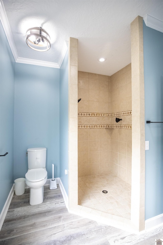 bathroom with a tile shower, toilet, ornamental molding, and wood-type flooring