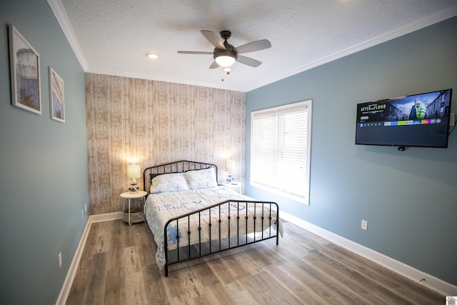 bedroom featuring a textured ceiling, ceiling fan, wooden walls, crown molding, and hardwood / wood-style floors