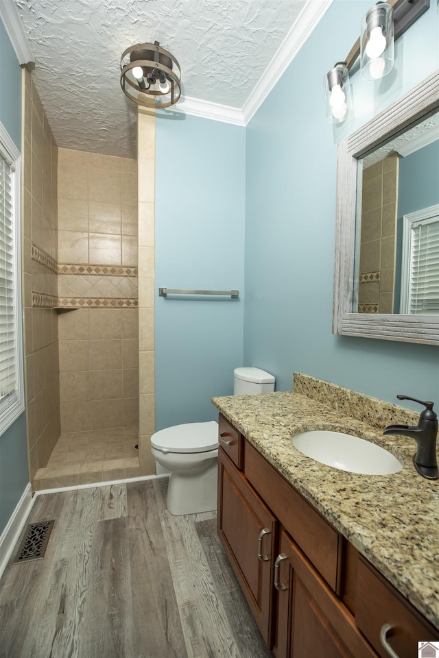 bathroom with crown molding, wood-type flooring, a textured ceiling, toilet, and tiled shower