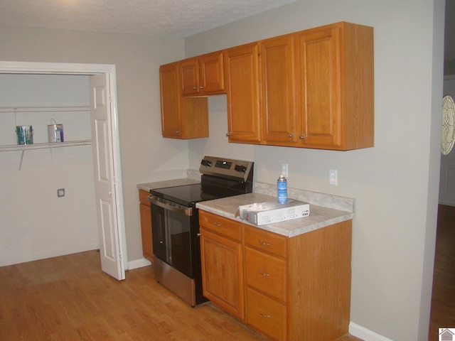 kitchen with a textured ceiling, light wood-type flooring, and stainless steel electric range