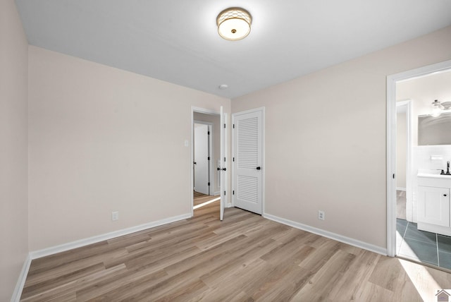 unfurnished bedroom featuring ensuite bathroom, sink, and light hardwood / wood-style floors