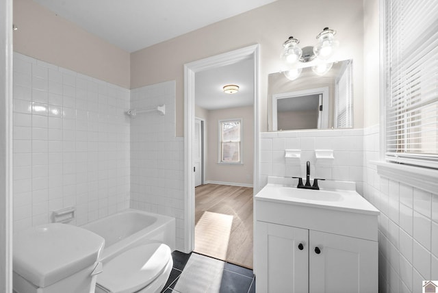 full bathroom featuring vanity, tile patterned floors, tiled shower / bath, toilet, and tile walls