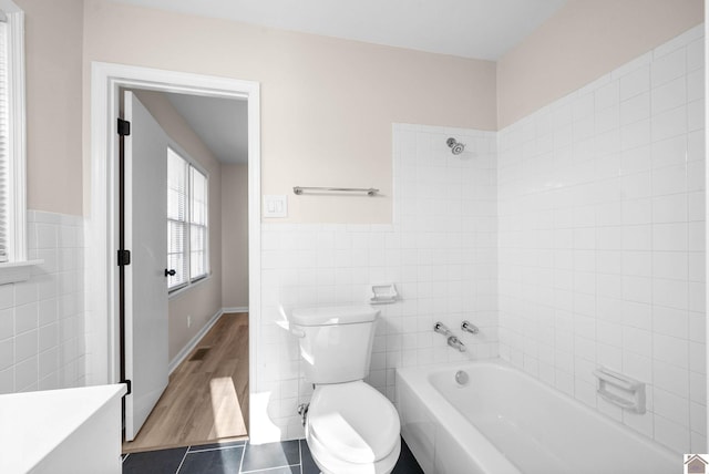 bathroom featuring tile patterned flooring, a tub to relax in, toilet, and tile walls