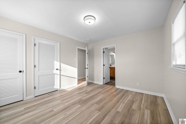 unfurnished bedroom with ensuite bath, multiple closets, and light hardwood / wood-style floors