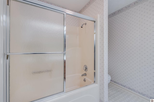 bathroom featuring toilet and shower / bath combination with glass door