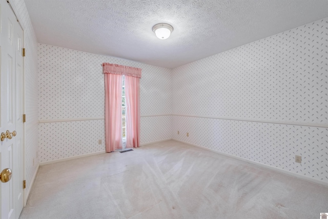 empty room with light colored carpet and a textured ceiling