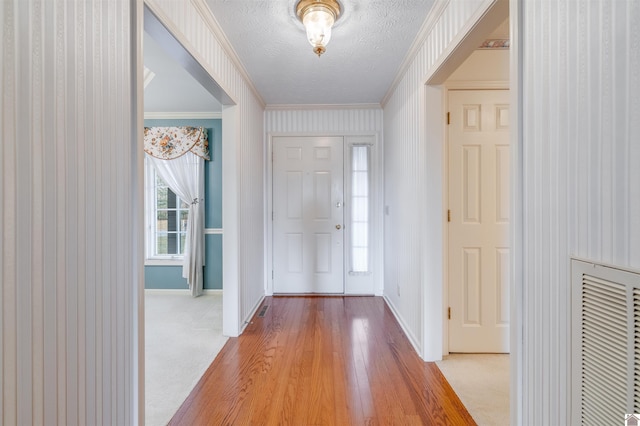 entryway with a textured ceiling, light hardwood / wood-style flooring, and ornamental molding