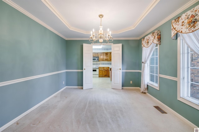 carpeted empty room featuring a tray ceiling, crown molding, and an inviting chandelier