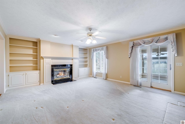 unfurnished living room featuring built in shelves, a textured ceiling, light colored carpet, ceiling fan, and crown molding