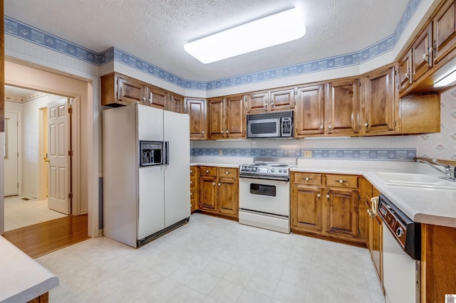 kitchen featuring a textured ceiling, white appliances, and sink