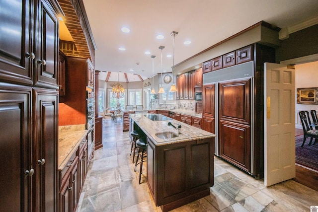 kitchen with a kitchen bar, light stone counters, sink, a center island with sink, and hanging light fixtures