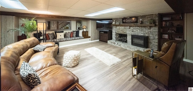 living room featuring a brick fireplace, a drop ceiling, and light hardwood / wood-style flooring