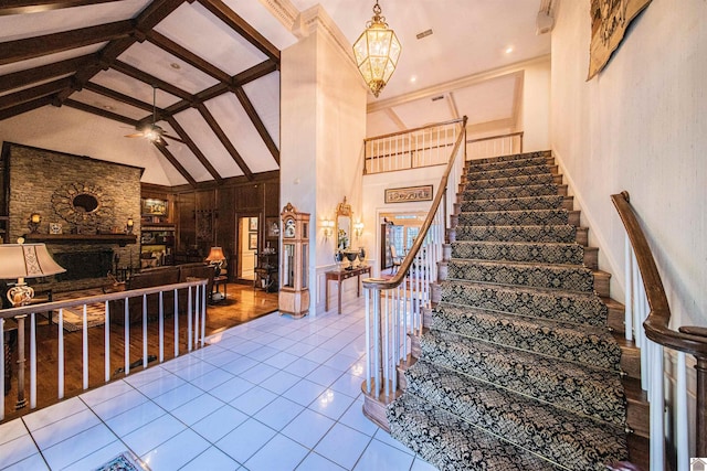 stairway with a stone fireplace, beamed ceiling, high vaulted ceiling, tile patterned floors, and ceiling fan with notable chandelier