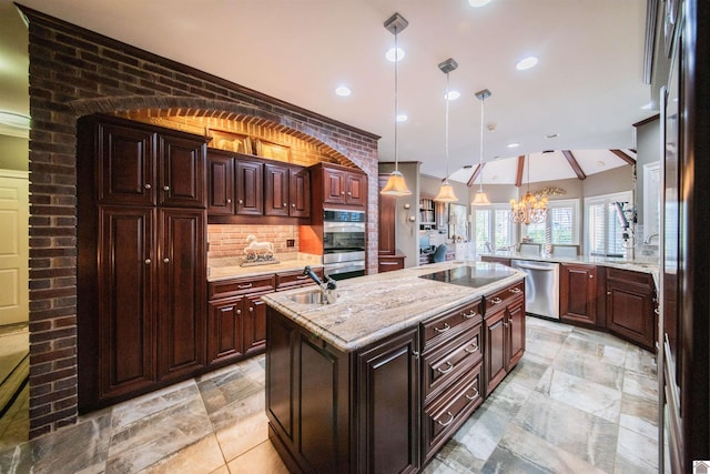 kitchen featuring sink, stainless steel appliances, hanging light fixtures, brick wall, and a kitchen island with sink