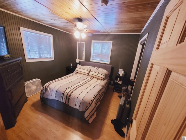 bedroom with ceiling fan, wood walls, light wood-type flooring, and ornamental molding