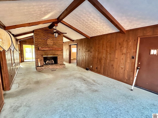 unfurnished living room featuring lofted ceiling with beams, wood walls, light colored carpet, a textured ceiling, and a fireplace