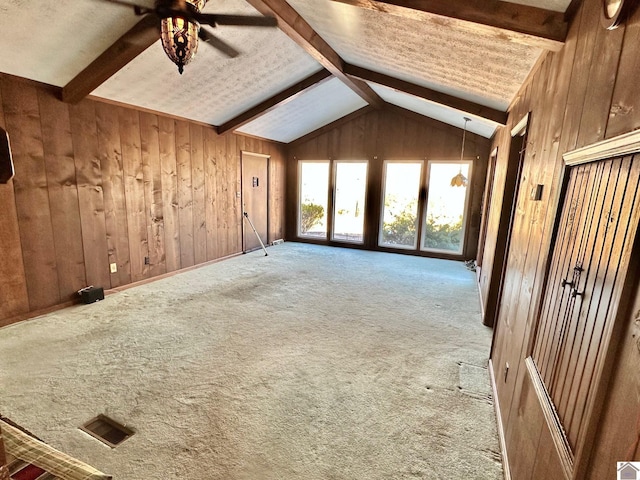 unfurnished living room with vaulted ceiling with beams, ceiling fan, carpet floors, and wood walls