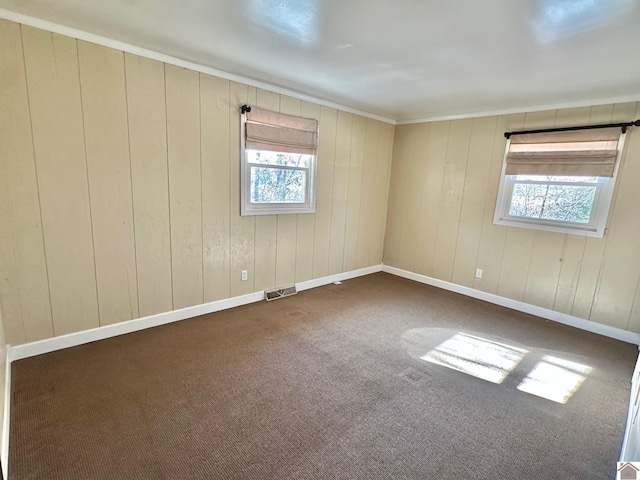 empty room with dark colored carpet, plenty of natural light, and wooden walls