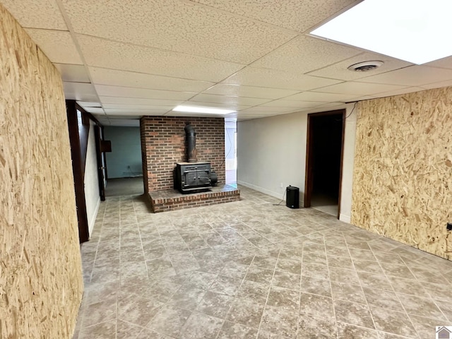 basement with a paneled ceiling and a wood stove