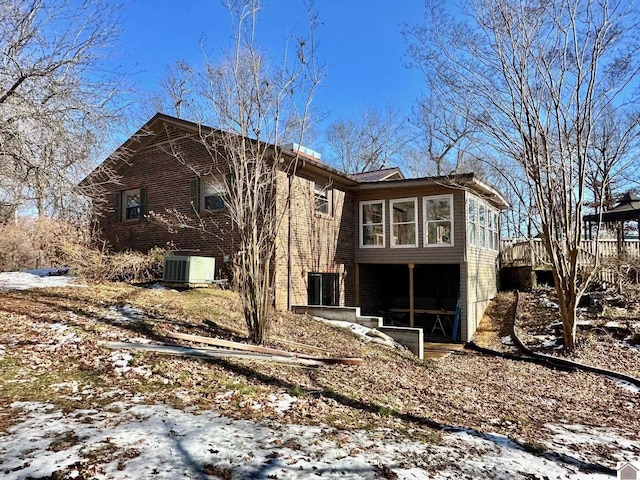 snow covered house featuring cooling unit and a sunroom