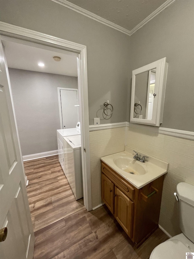 bathroom featuring washing machine and dryer, hardwood / wood-style floors, toilet, tile walls, and ornamental molding