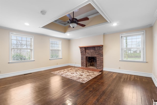 unfurnished living room featuring ceiling fan, a brick fireplace, a raised ceiling, dark hardwood / wood-style floors, and crown molding