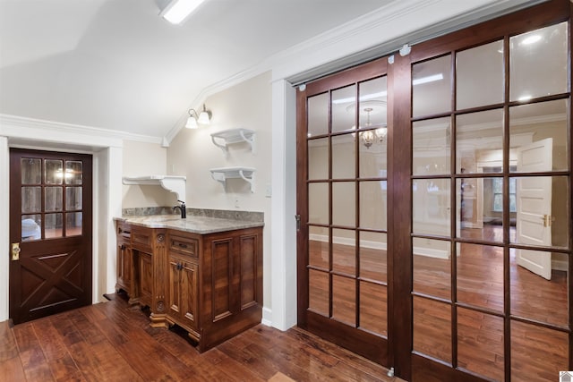 bar featuring dark hardwood / wood-style flooring, a chandelier, vaulted ceiling, and ornamental molding