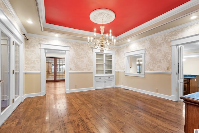 unfurnished dining area with hardwood / wood-style flooring, a notable chandelier, a raised ceiling, and ornamental molding