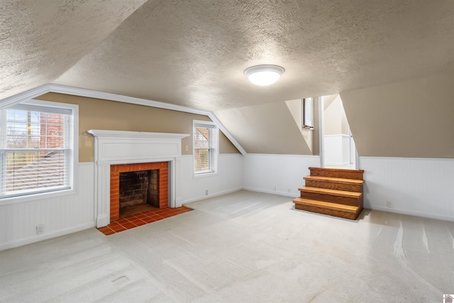 additional living space with a textured ceiling, light carpet, a fireplace, and vaulted ceiling