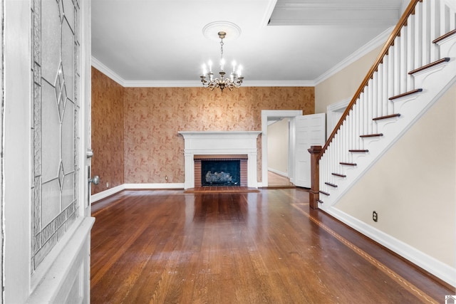 unfurnished living room with a brick fireplace, dark hardwood / wood-style flooring, a notable chandelier, and ornamental molding