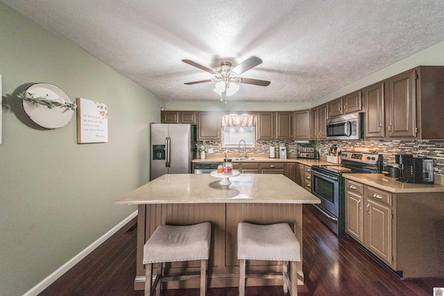 kitchen with a center island, backsplash, sink, ceiling fan, and appliances with stainless steel finishes