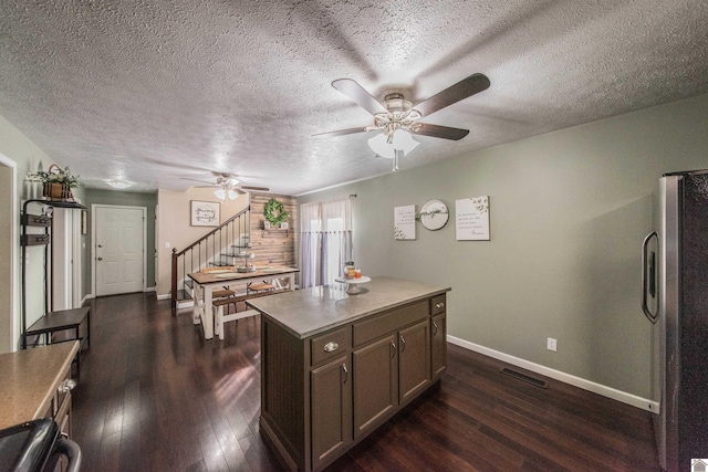 kitchen with a textured ceiling, dark hardwood / wood-style floors, a kitchen island, and stainless steel refrigerator