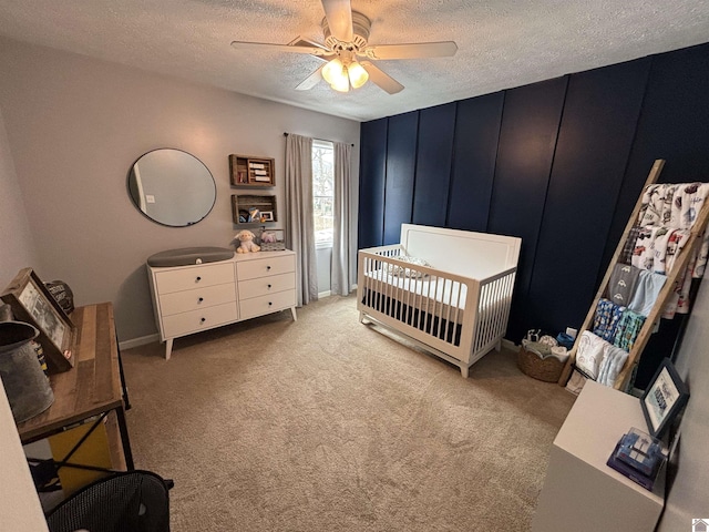 bedroom featuring a crib, a textured ceiling, light colored carpet, and ceiling fan