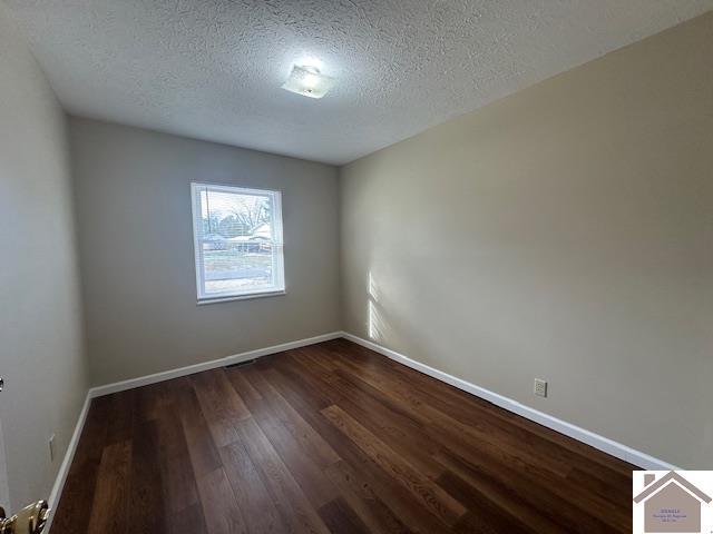 empty room with dark hardwood / wood-style floors and a textured ceiling