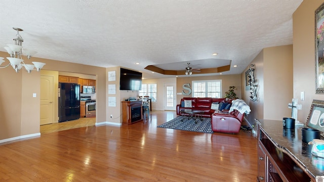 living room featuring a textured ceiling, light hardwood / wood-style floors, a raised ceiling, and ceiling fan with notable chandelier