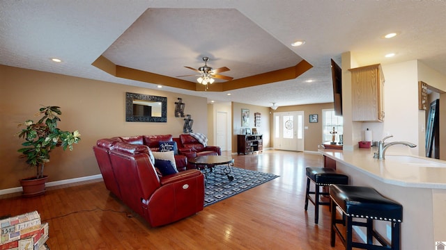 living room featuring hardwood / wood-style floors, ceiling fan, a tray ceiling, and sink