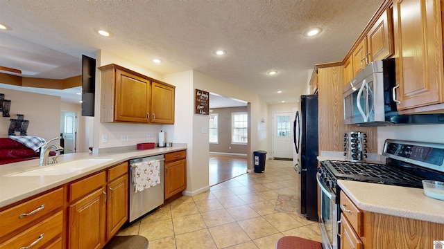 kitchen with a textured ceiling, appliances with stainless steel finishes, light tile patterned floors, and sink