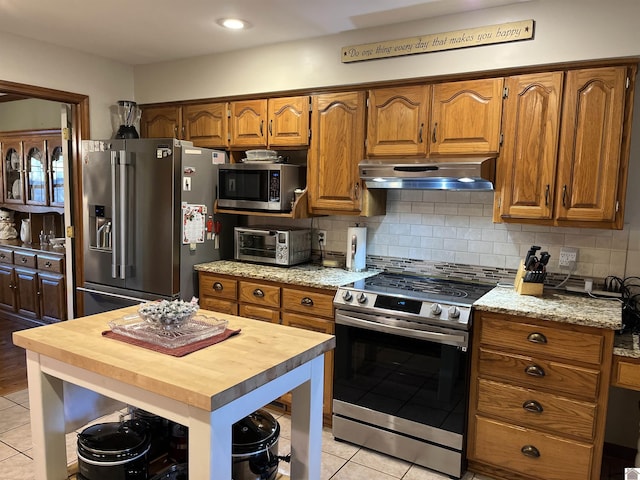 kitchen with light tile patterned floors, backsplash, appliances with stainless steel finishes, and wooden counters