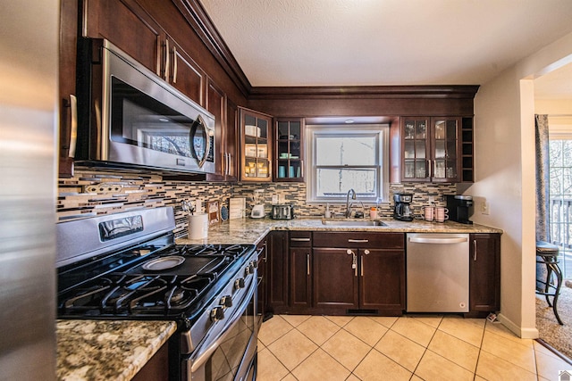 kitchen with light stone counters, appliances with stainless steel finishes, dark brown cabinets, and sink