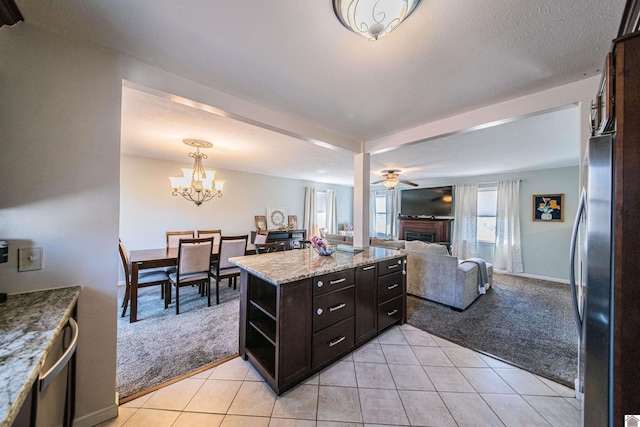 kitchen featuring light carpet, stainless steel refrigerator, light stone counters, dark brown cabinets, and ceiling fan with notable chandelier