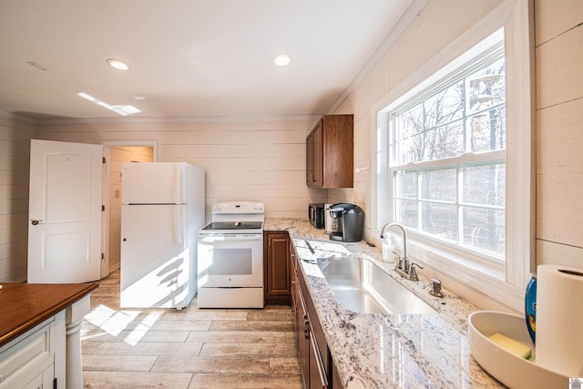 kitchen with white appliances, wooden walls, light stone counters, and sink