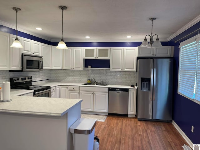 kitchen with appliances with stainless steel finishes, kitchen peninsula, pendant lighting, white cabinets, and sink