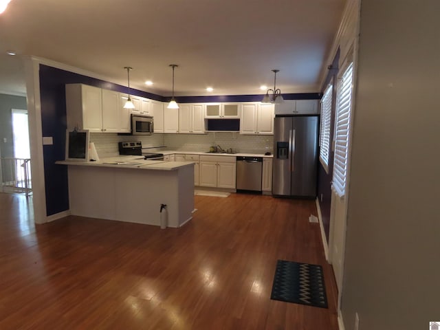 kitchen with kitchen peninsula, hanging light fixtures, dark hardwood / wood-style flooring, white cabinetry, and appliances with stainless steel finishes